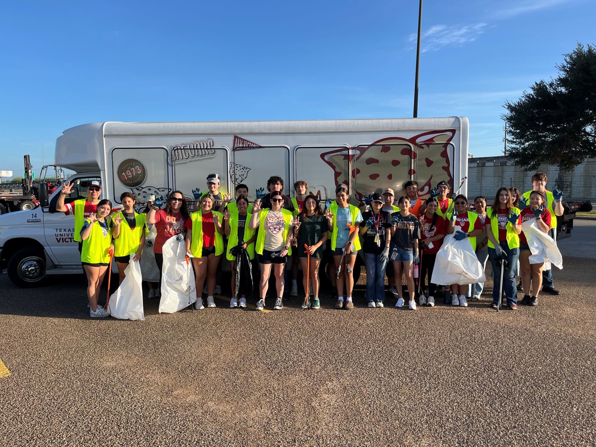 A group of students in reflective vests stand in front of a university shuttle bus.