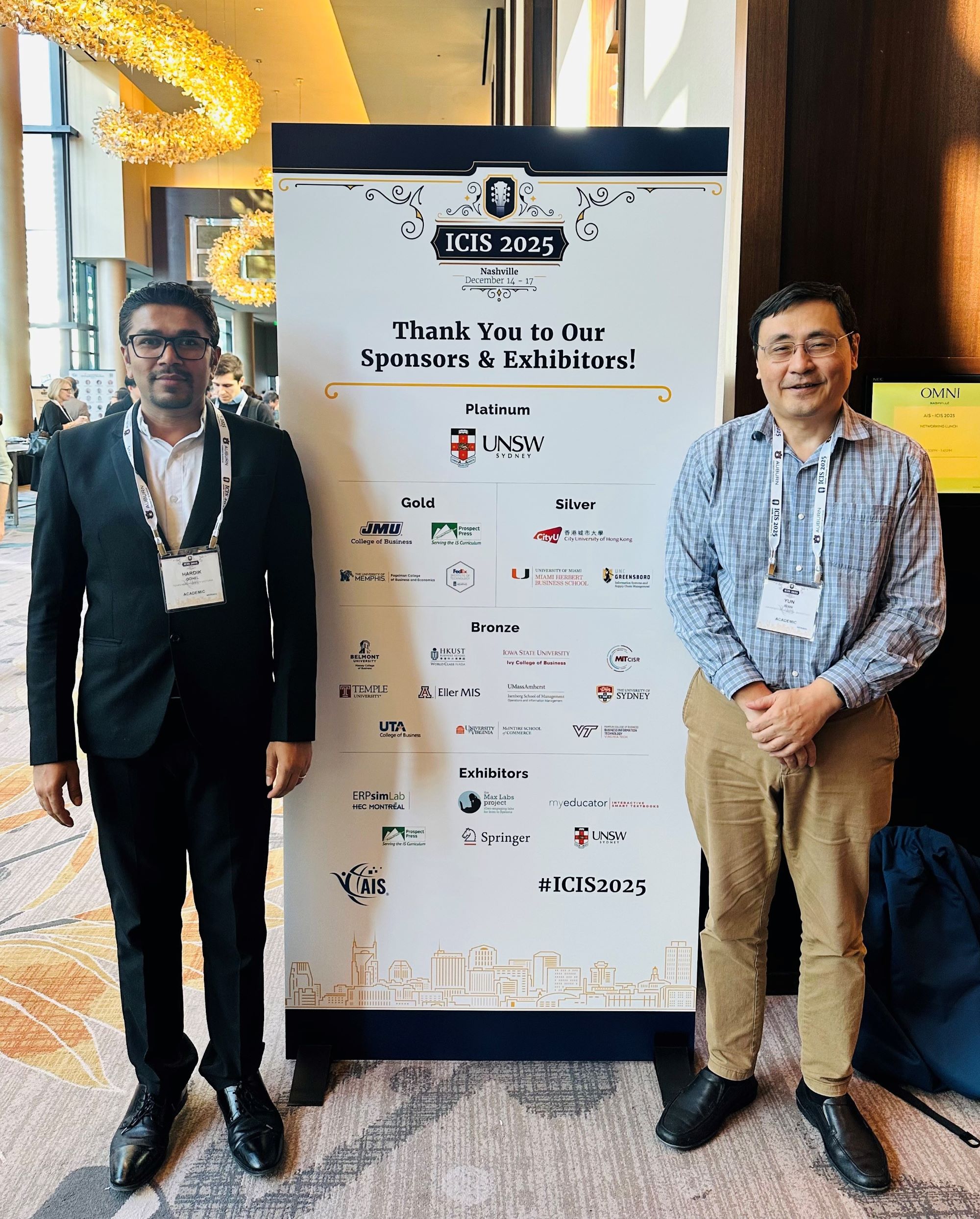 Hardik Gohel and Yun Wan stand with a banner for the International Conference on Information Systems.