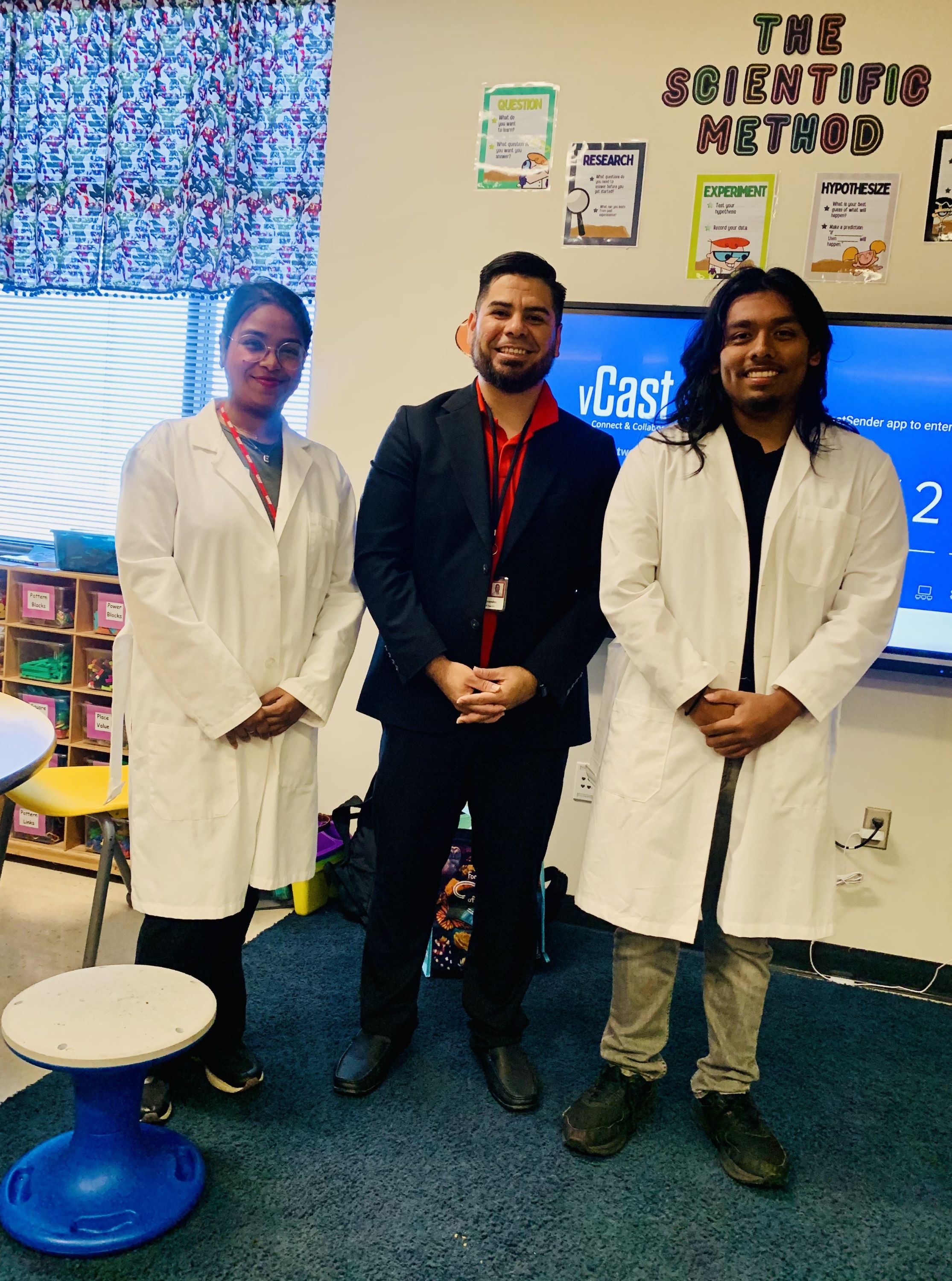 Two students and a faculty member pose in an elementary school classroom.