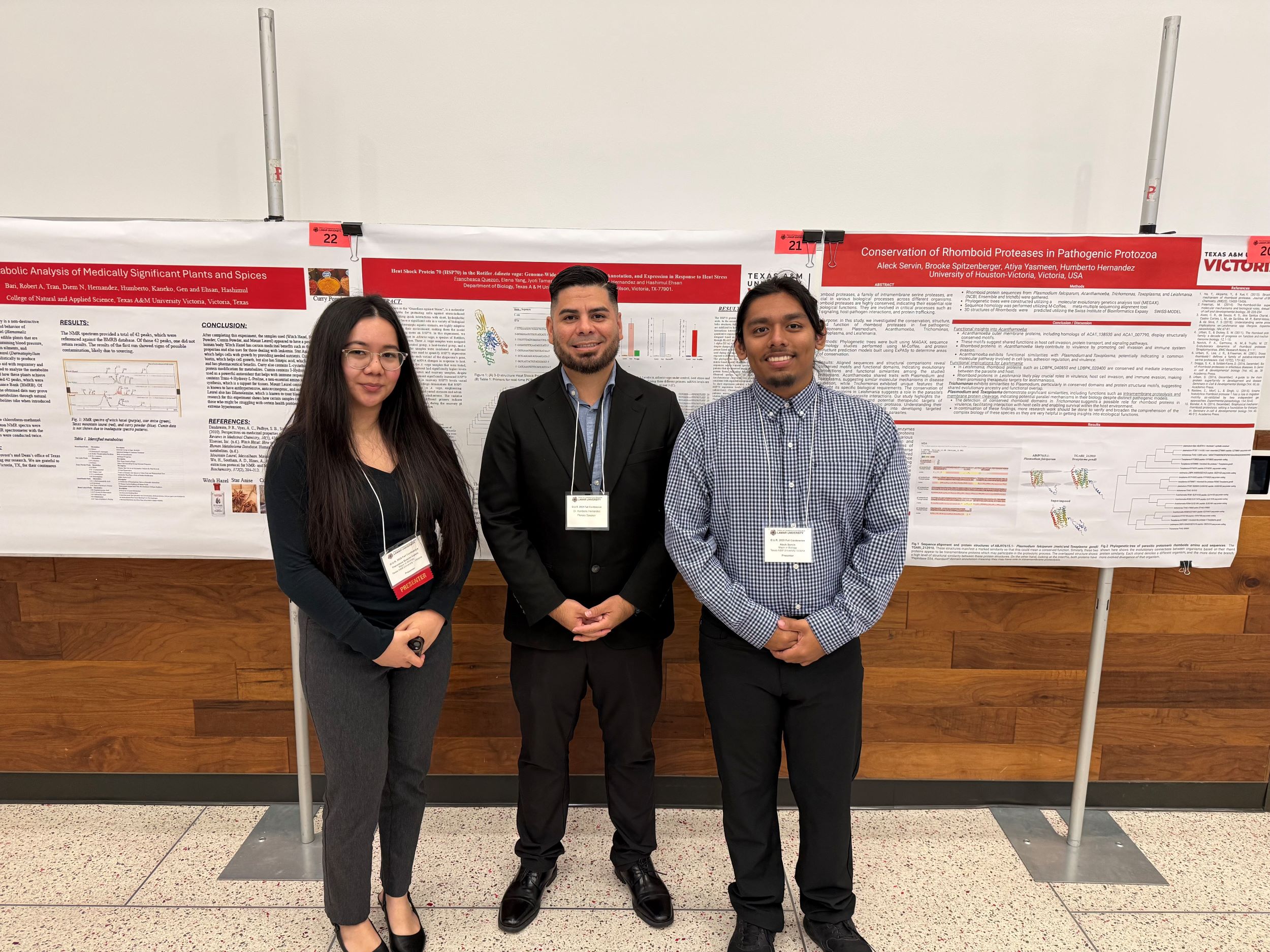 Two students and a faculty member stand in front of research posters at a conference.