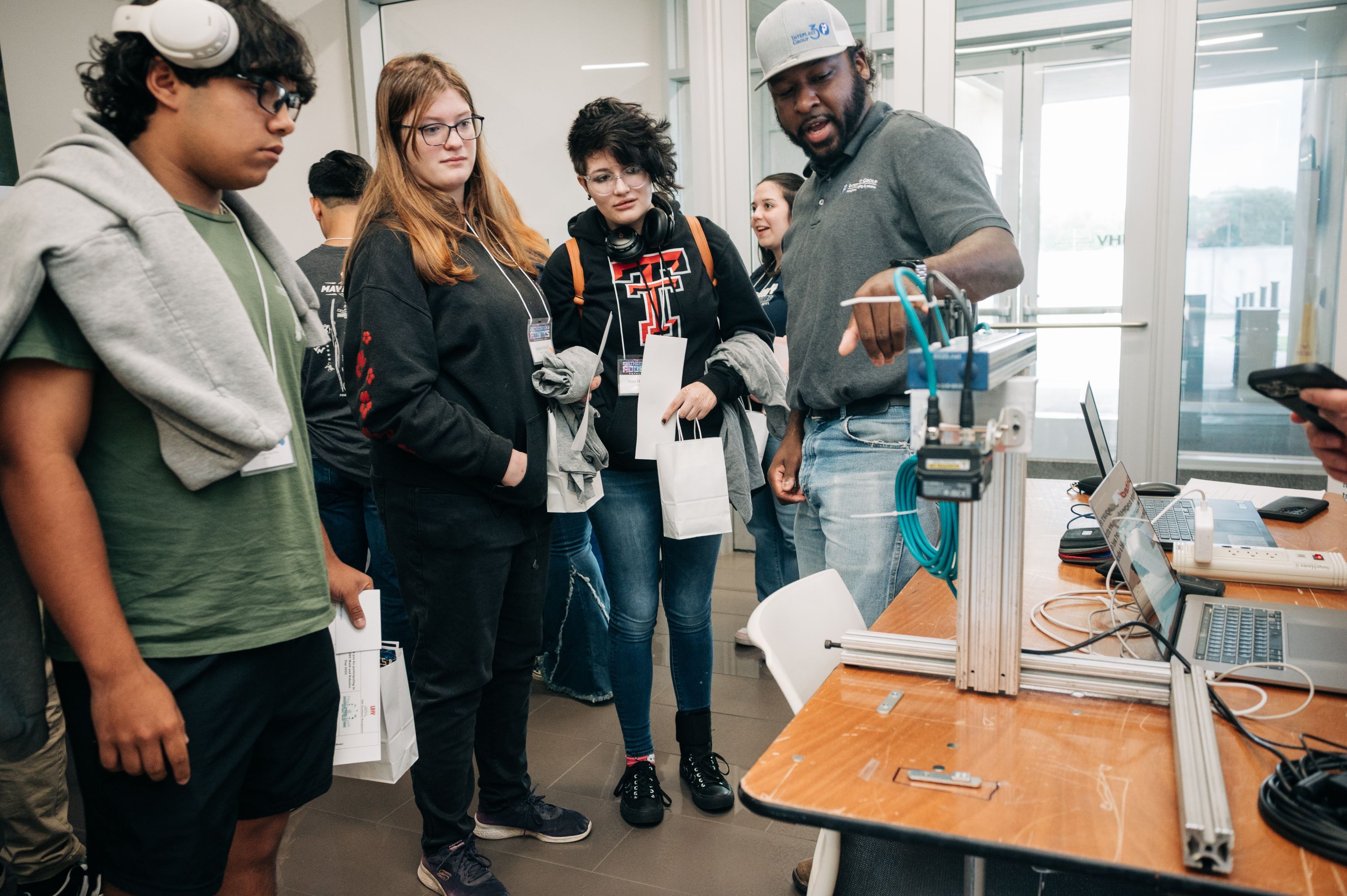 A group of students listen to a man talk about a piece of equipment.