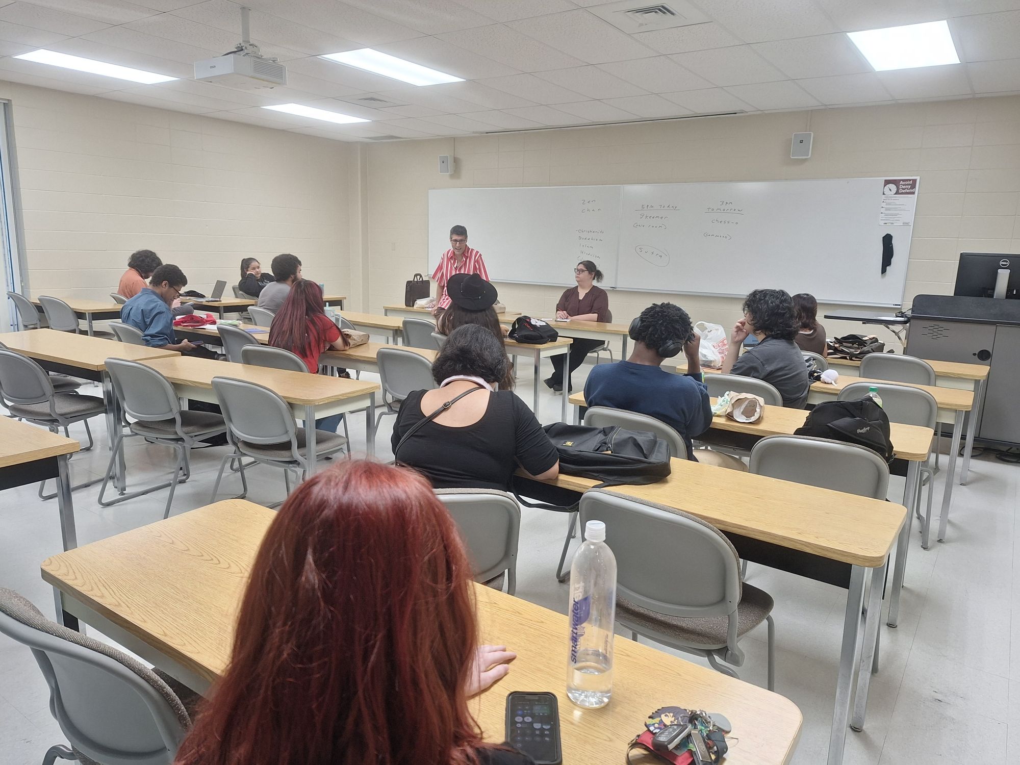 A room full of students listen to a male teacher speak.